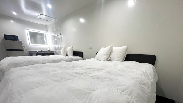 A hotel room with two large beds, a small desk, a mirror, and a window. - Newport Bay Inn (Costa Mesa)