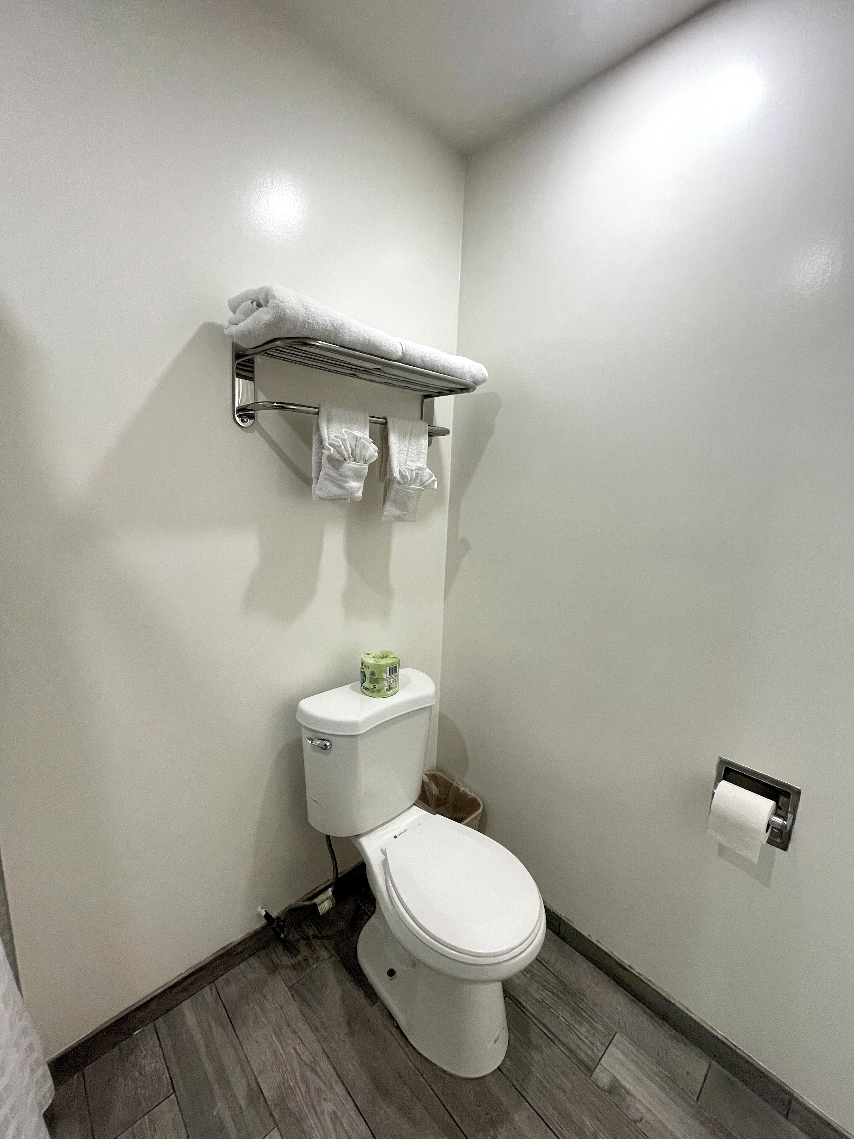 A bathroom with a toilet, a towel rack with towels, a toilet paper holder, and a trash bin.