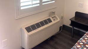 A room with a large window with blinds, a wall-mounted air conditioner, and a small table. - Newport Bay Inn (Costa Mesa)