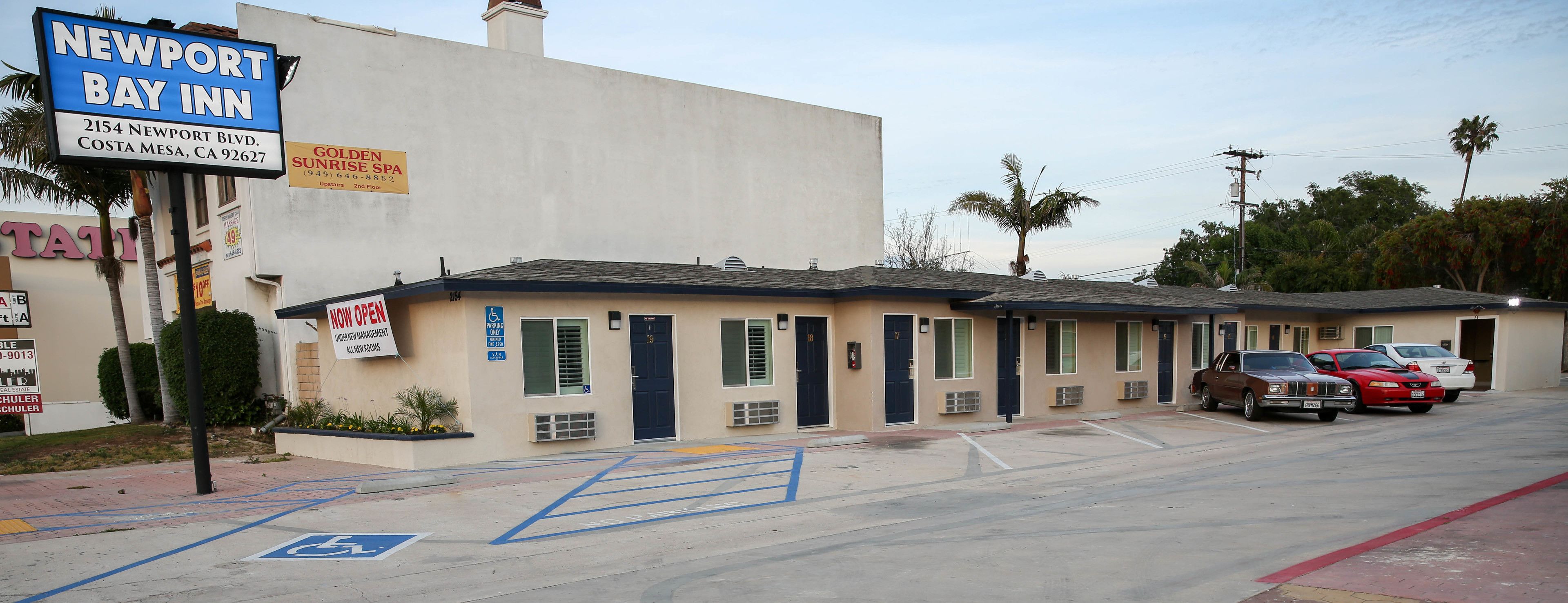 A motel with a sign for Newport Bay Inn, a parking lot, and several cars parked in front.