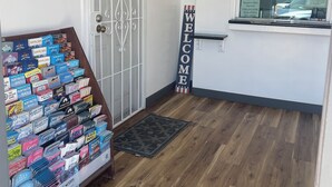 A hotel reception area with a 'WELCOME' sign, a display of travel guides, and a security camera. - Newport Bay Inn (Costa Mesa)