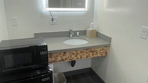A small bathroom with a sink, mirror, and a microwave. - Newport Bay Inn (Costa Mesa)