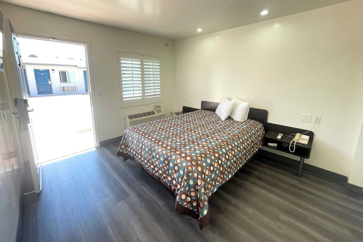A bedroom with a bed, a bedside table, a phone, and a window with blinds.