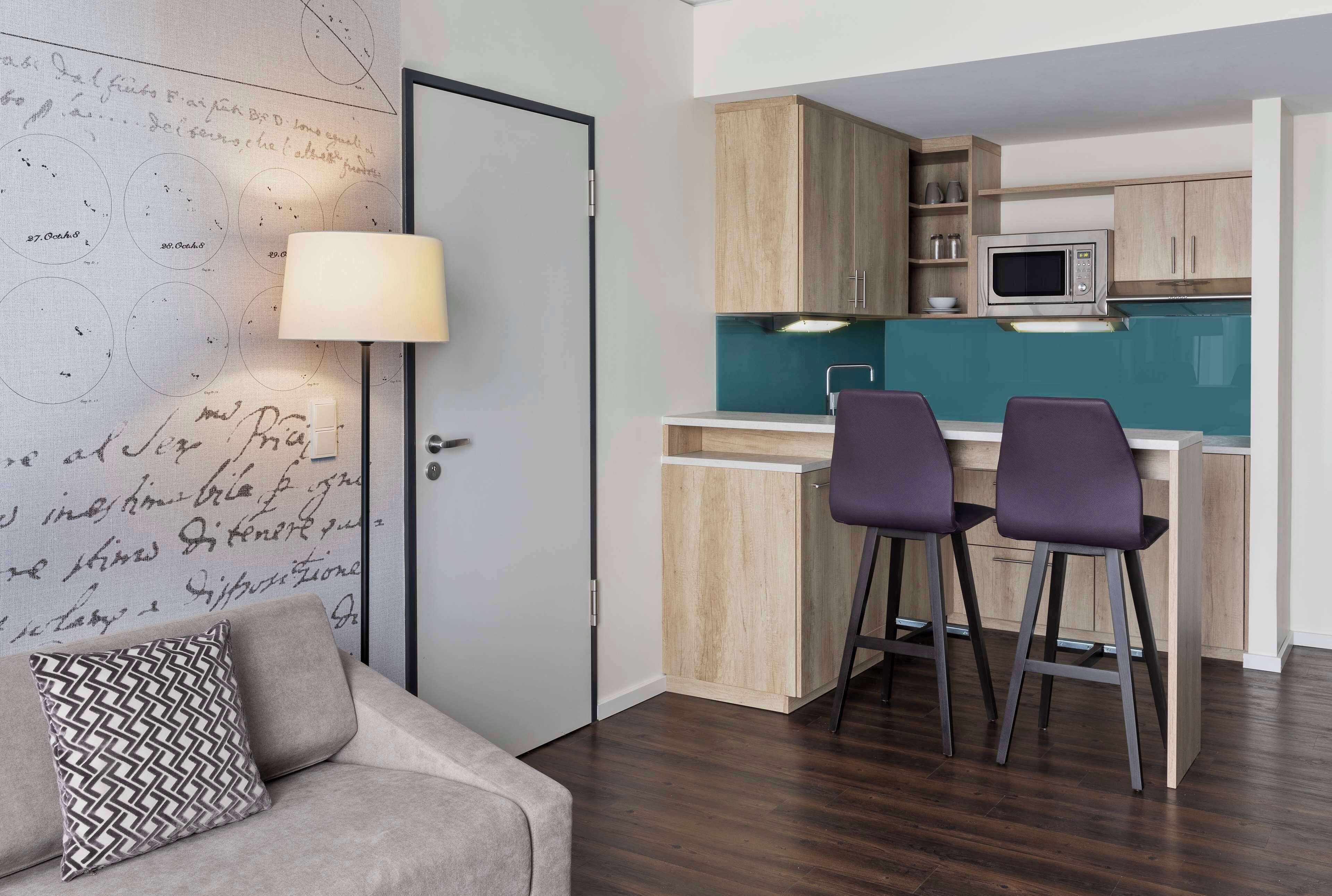 A compact living space with a kitchenette, a sofa with patterned cushions, and a bar area with stools.