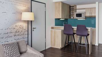 A compact living space with a kitchenette, a sofa with patterned cushions, and a bar area with stools.