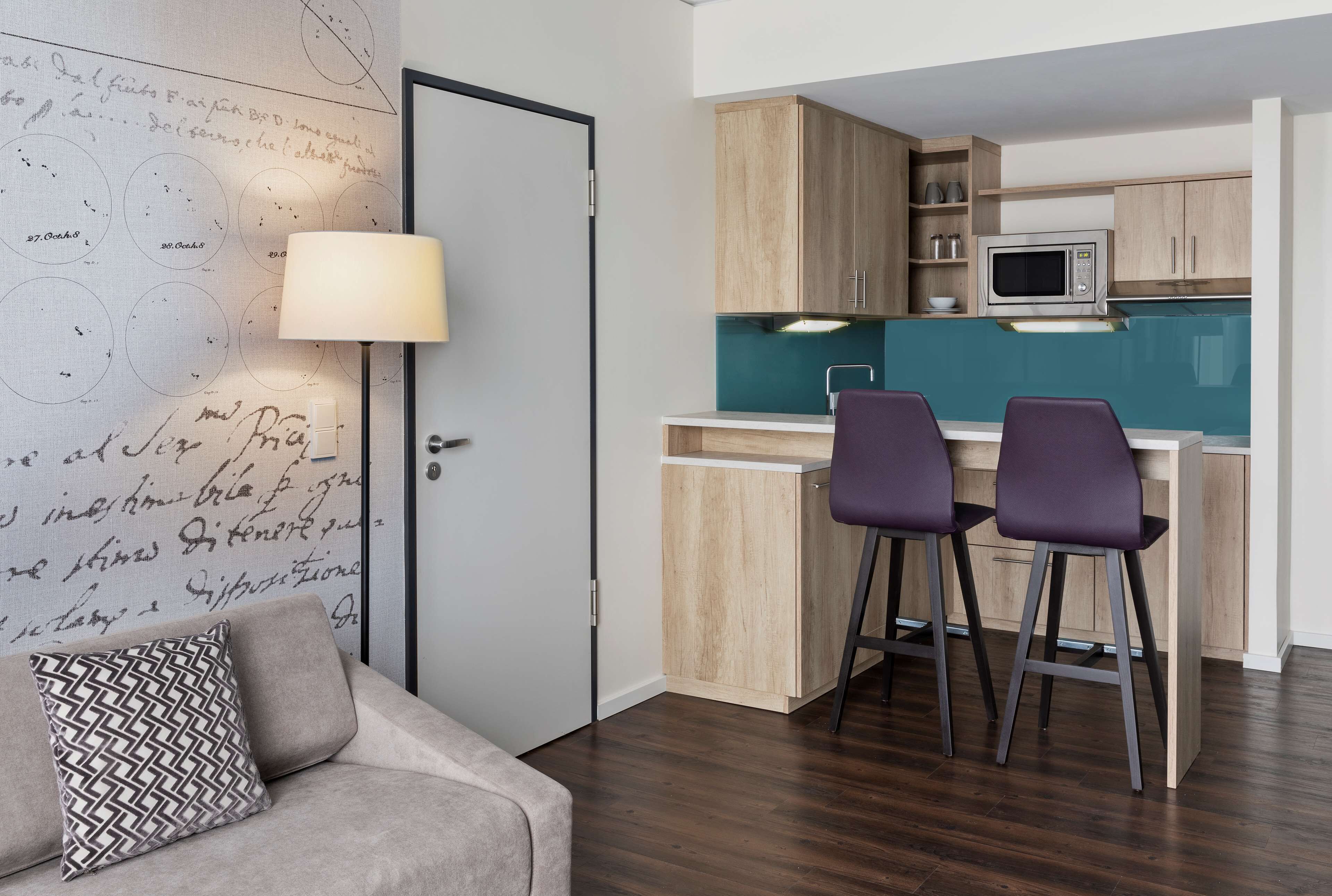 A compact kitchen with wooden cabinets, a microwave, and two bar stools.