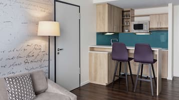A compact kitchen with wooden cabinets, a microwave, and two bar stools.