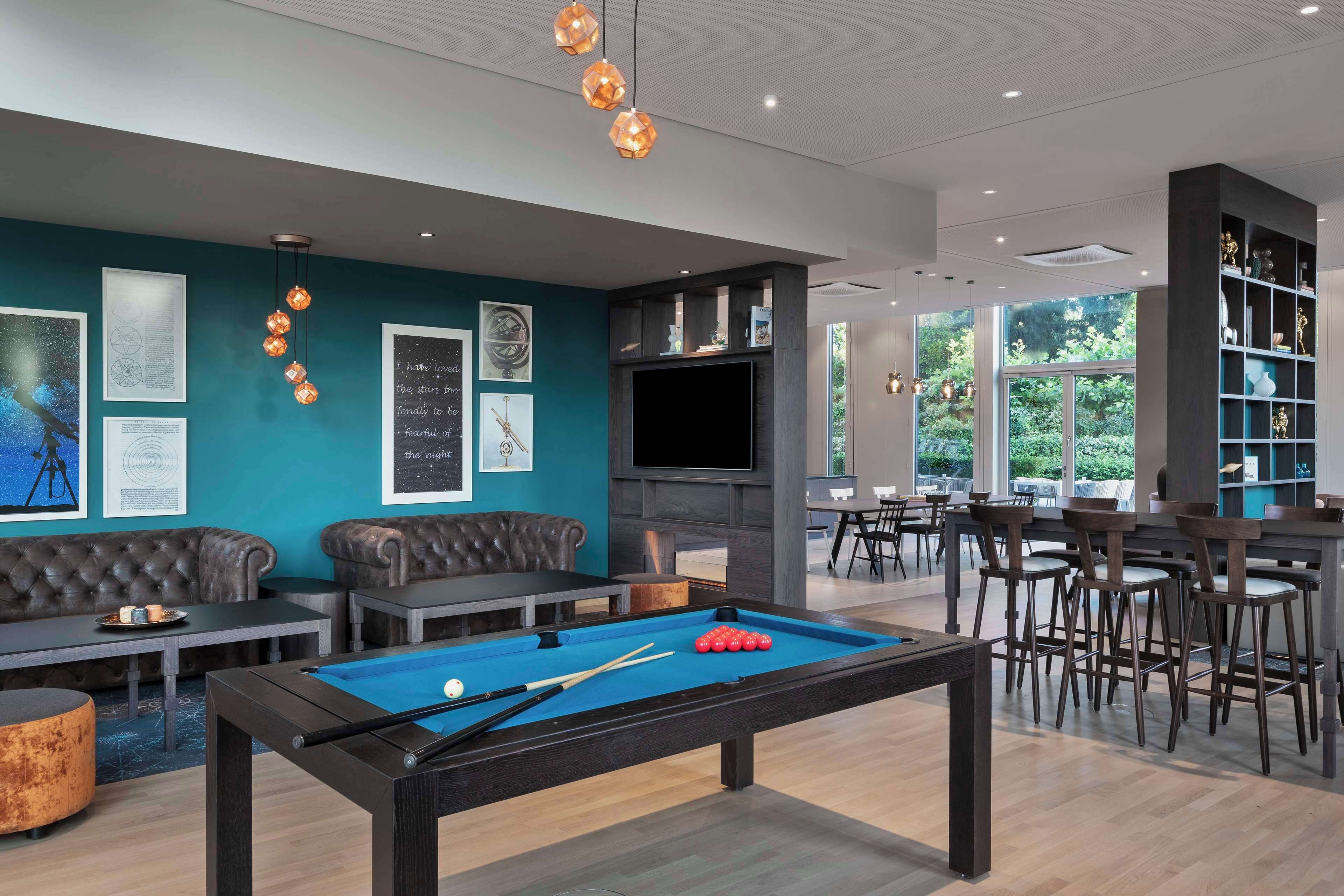 A pool table with a billiard cue and balls, a sofa, a television, and a bar area with chairs.