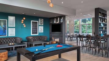 A pool table with a billiard cue and balls, a sofa, a television, and a bar area with chairs.