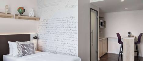Una habitación de hotel moderna con una gran pared llena de notas escritas a mano, una cama con almohadas estampadas, un globo terráqueo y una pequeña estatua en un estante.
