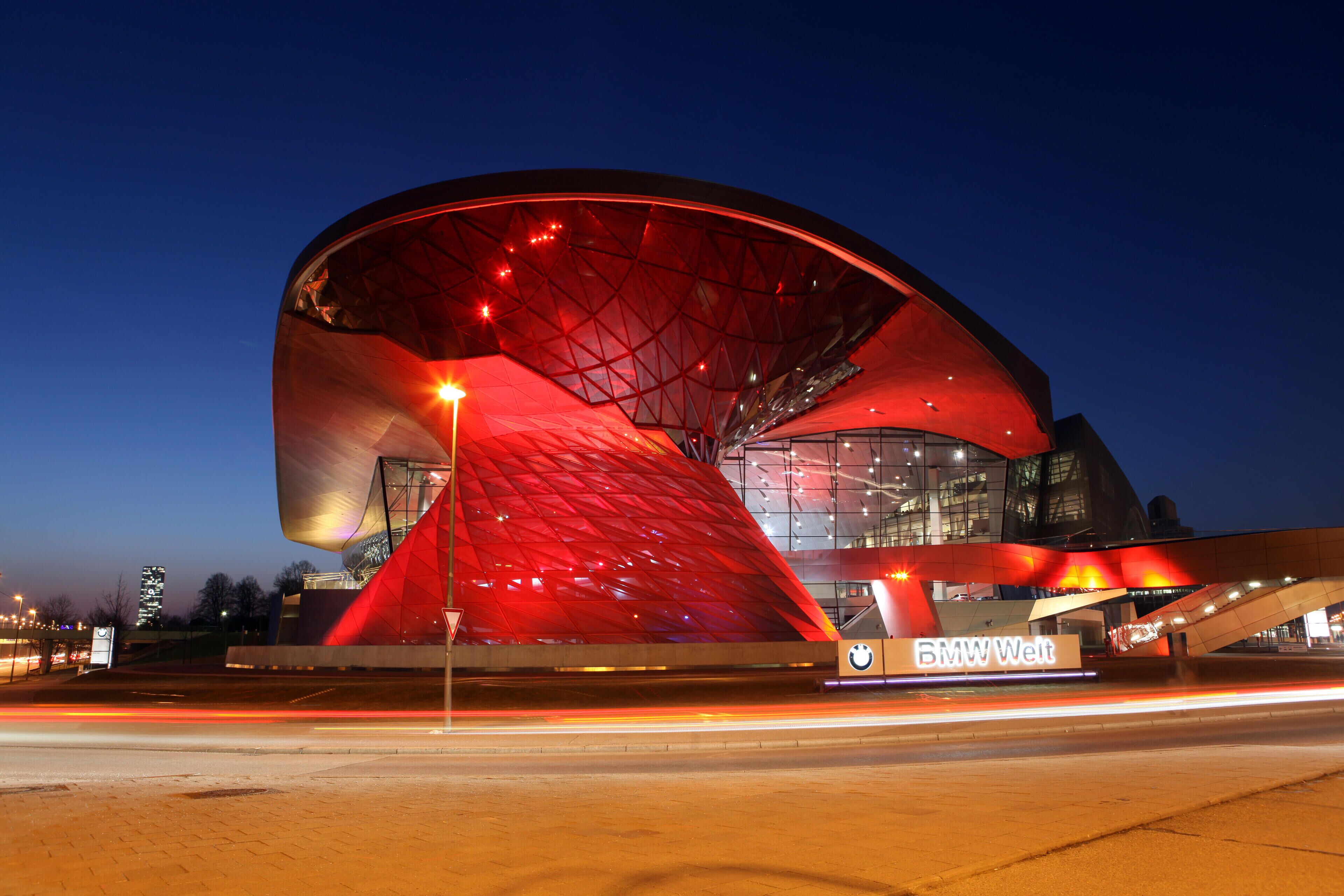 Een modern gebouw met een opvallend rood dak en glazen gevel, met het logo van BMW Welt.