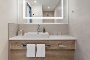 Un baño moderno con lavamanos blanco, espejo y tocador de madera.
