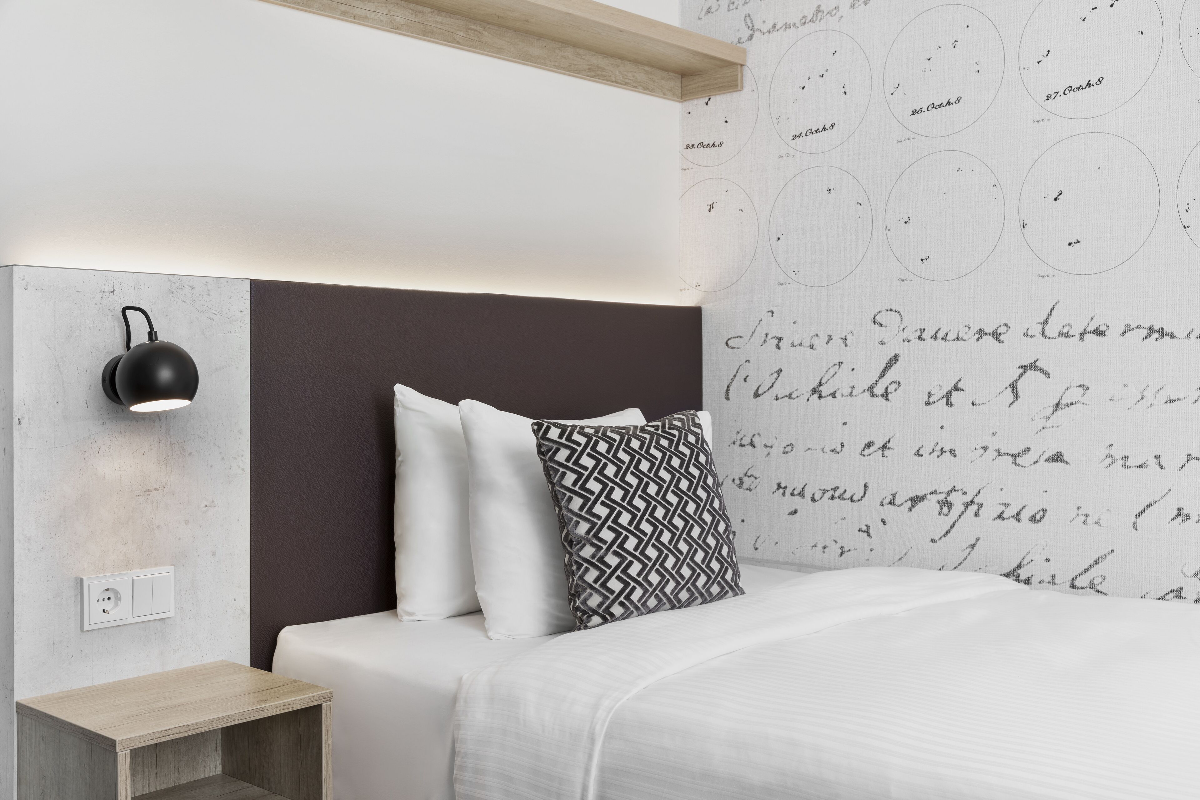 Un dormitorio moderno con cama, mesita de noche, lámpara de pared y un diseño decorativo en la pared con motivos circulares.