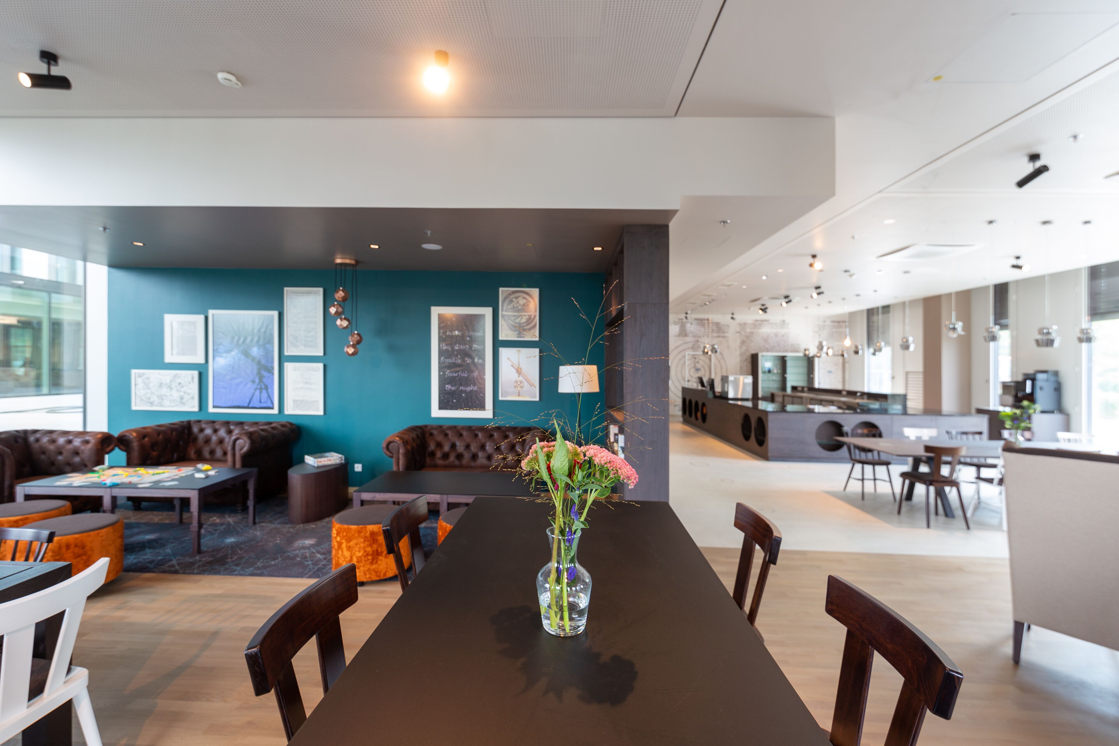 A modern interior with a long dining table, comfortable seating, and a kitchen area.