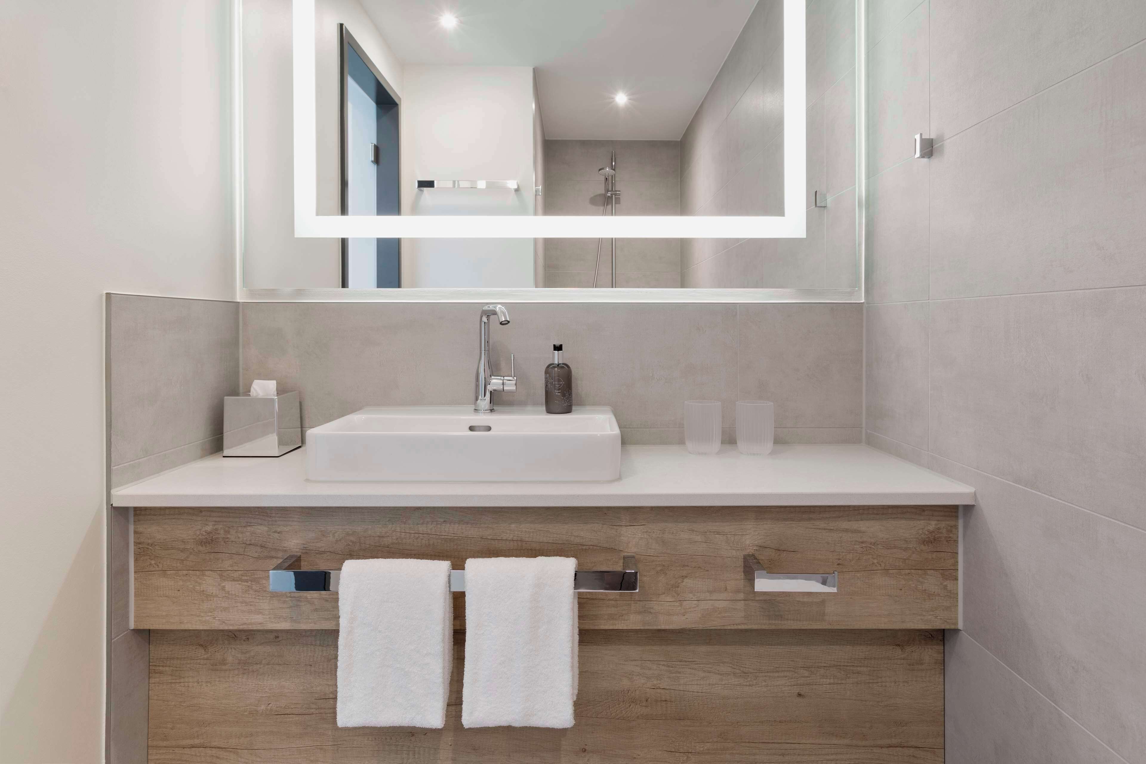 A modern bathroom with a white sink, a large mirror, and wooden cabinetry.