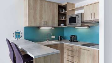 A compact kitchen with wooden cabinets, a microwave, a sink, and a coffee maker.