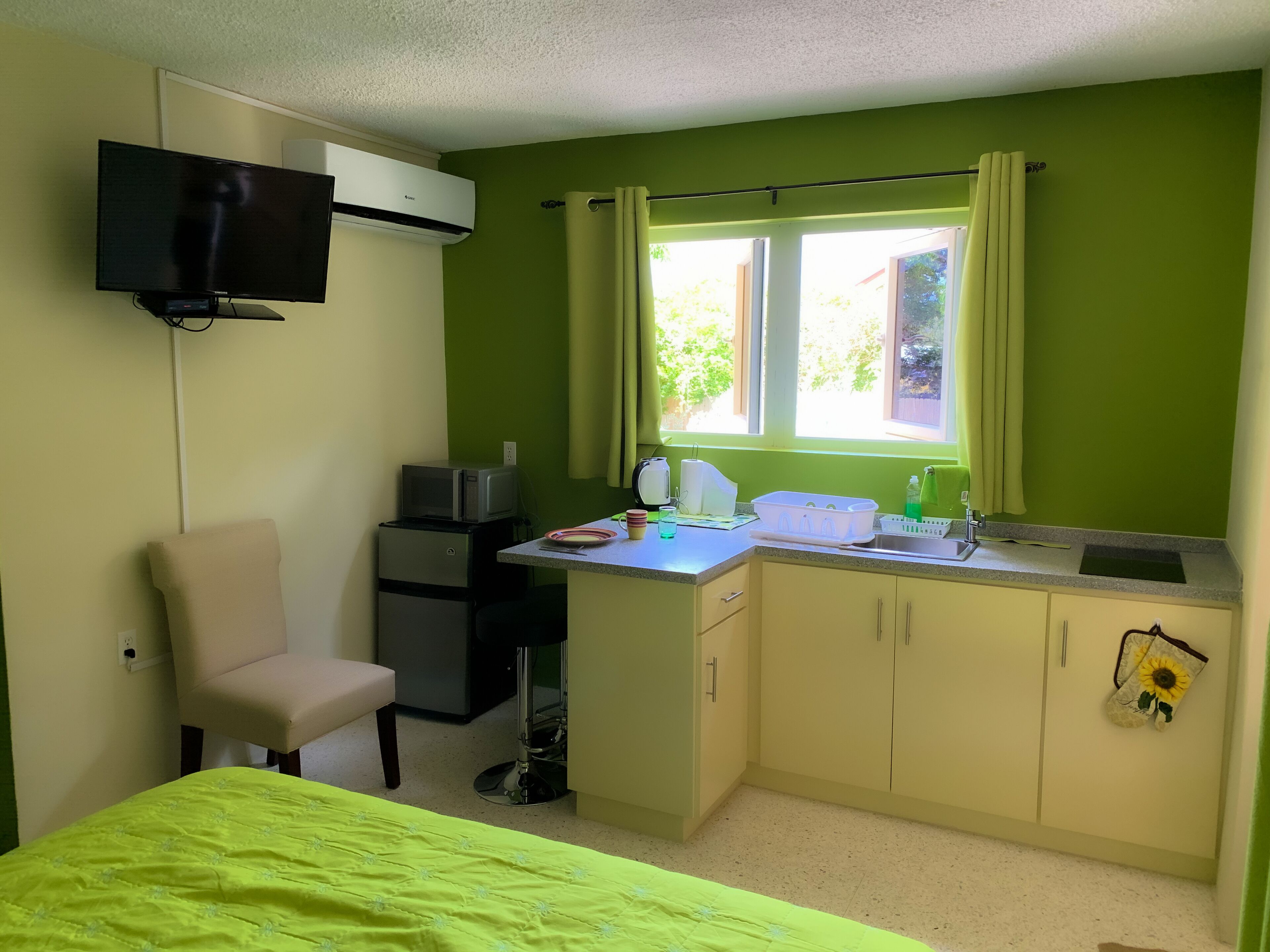 A compact room with a bed, a desk with a computer, a microwave, and a small kitchenette.