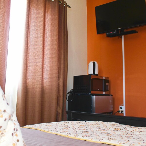 Une chambre d’hôtel équipée d’un lit, d’un téléviseur à écran plat fixé au mur, d’une machine à café et d’un four à micro-ondes posé sur une petite table.