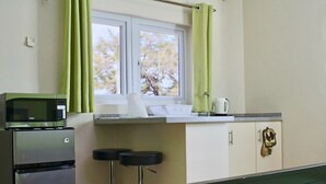 Een kleine keuken met een magnetron, koelkast en raam voorzien van gordijnen.