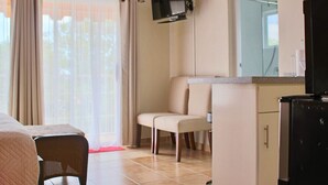 Een hotelkamer met een bed, een aan de muur bevestigde televisie, een zithoek met stoelen en een kitchenette.