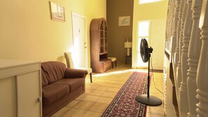 Un salon avec un canapé marron, un meuble en bois, un ventilateur et un tapis à motifs.