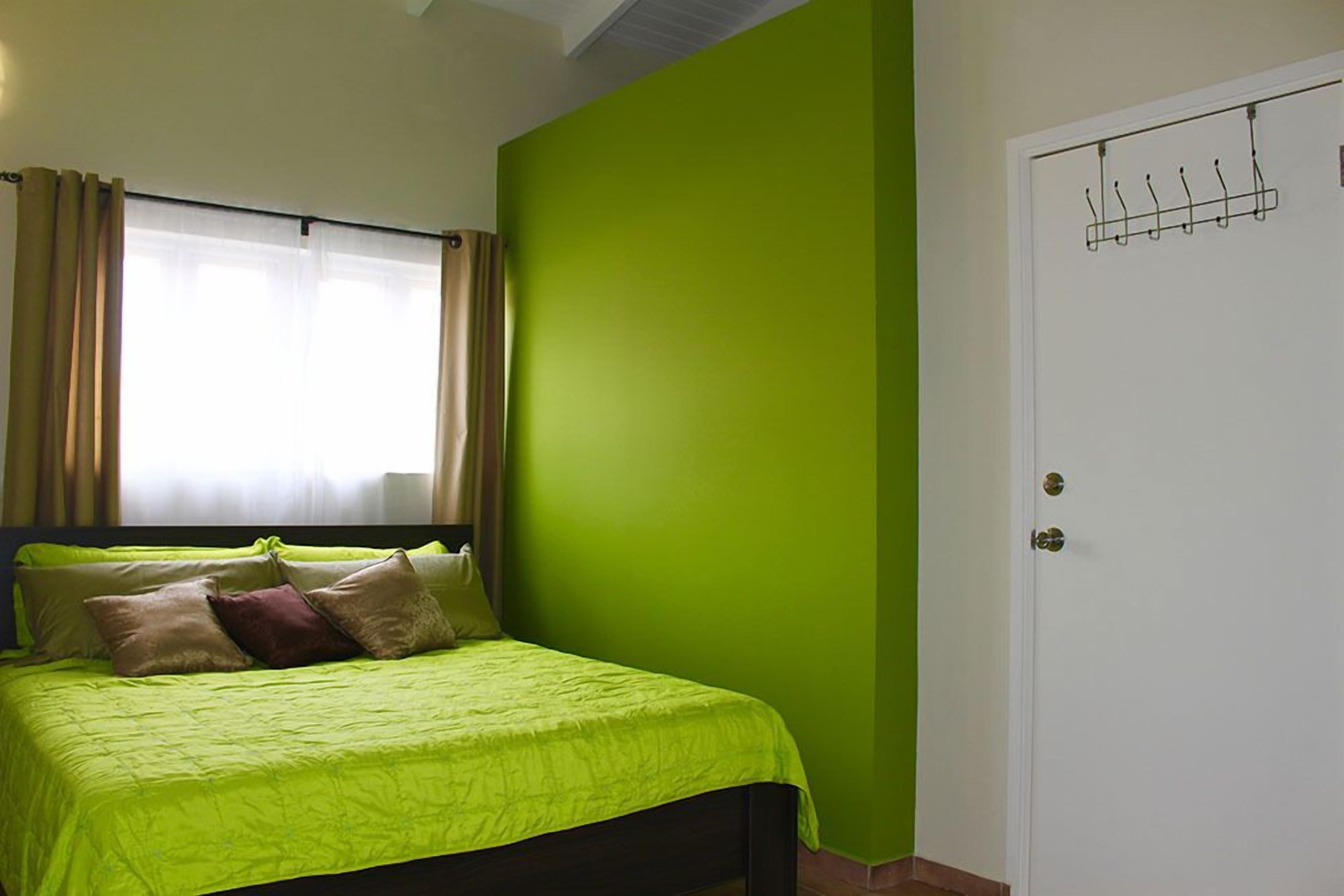 A bedroom with a bed, green walls, a white door, and a window with curtains.