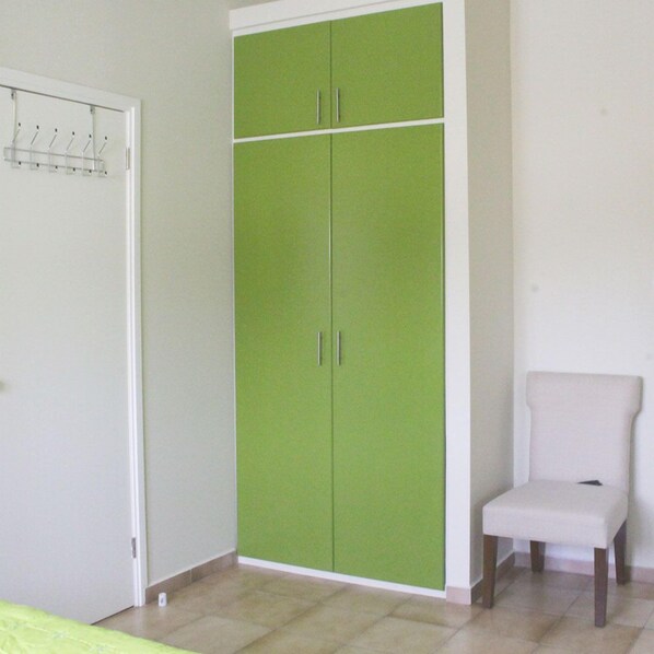 A room with a green wardrobe, a white chair, and a door with a coat rack.
