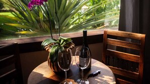 A table with a bottle of wine and two glasses, a vase with a plant, and a view of a mountainous landscape through a window.