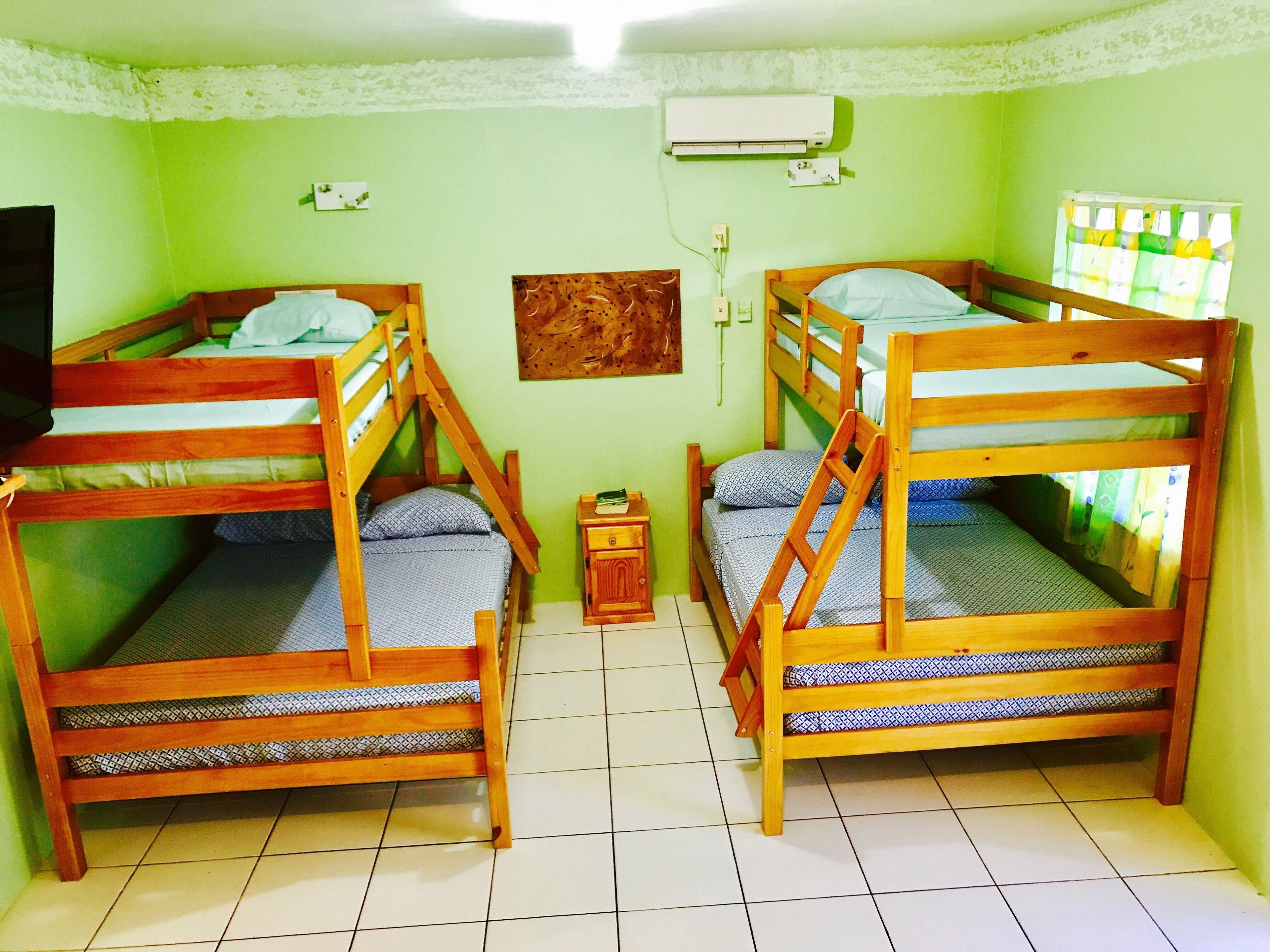 A room with two bunk beds, a small wooden nightstand, a wall-mounted air conditioner, and a window with curtains.