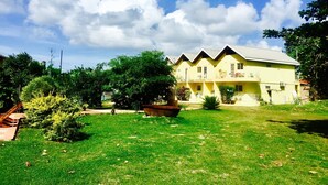 A yellow building with a flat roof, labeled "Crooks Apartments," surrounded by greenery and a clear sky. - BAGOS ECO RETREAT & CAFE (Crown Point)
