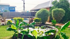 A garden with a pond surrounded by banana plants and a wooden fence. - BAGOS ECO RETREAT & CAFE (Crown Point)
