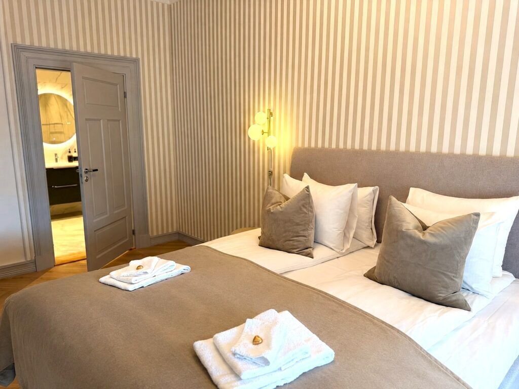 Een hotelkamer met een bed, kussens, een bedlamp en een deur naar een badkamer.