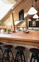 Una zona de bar con taburetes, una cocina al fondo y un tragaluz.