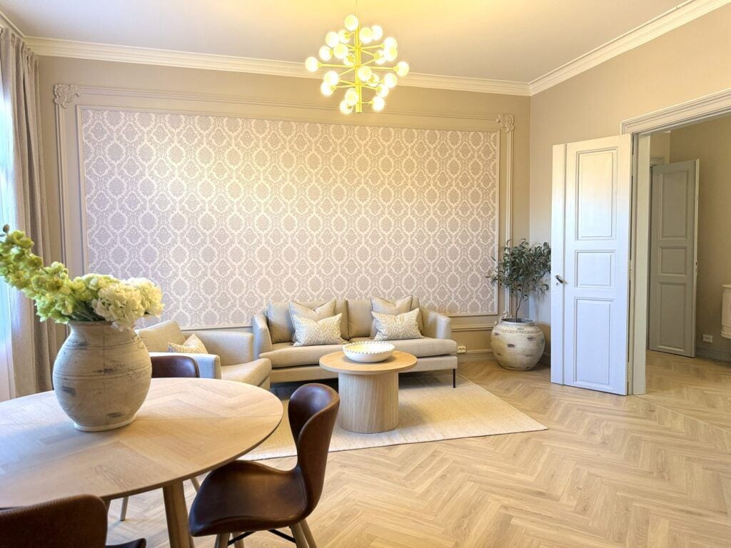 Sala de estar com sofá, mesa de jantar com cadeiras, um vaso decorativo e papel de parede estampado.