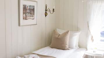 A single bed with a beige blanket, a framed picture on the wall, and a small table with a candle.