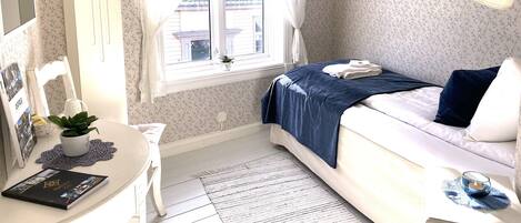 A bedroom with a bed, bedside table, lamp, and window with curtains.