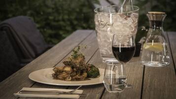 A wooden table with a plate of food, a glass of red wine, and a bottle of Freixenet rosé.