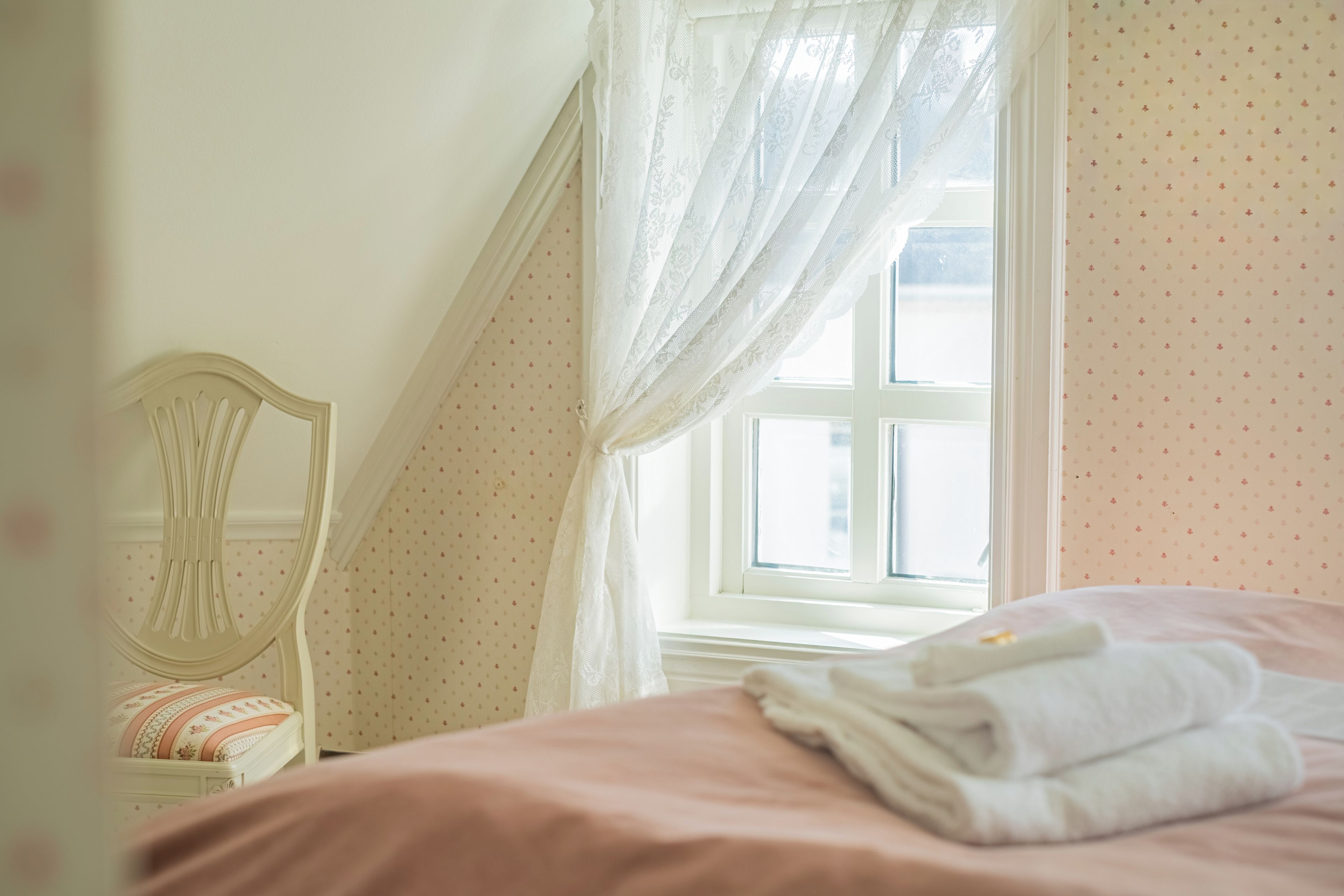 Un dormitorio con cama, una silla y una ventana con cortinas.