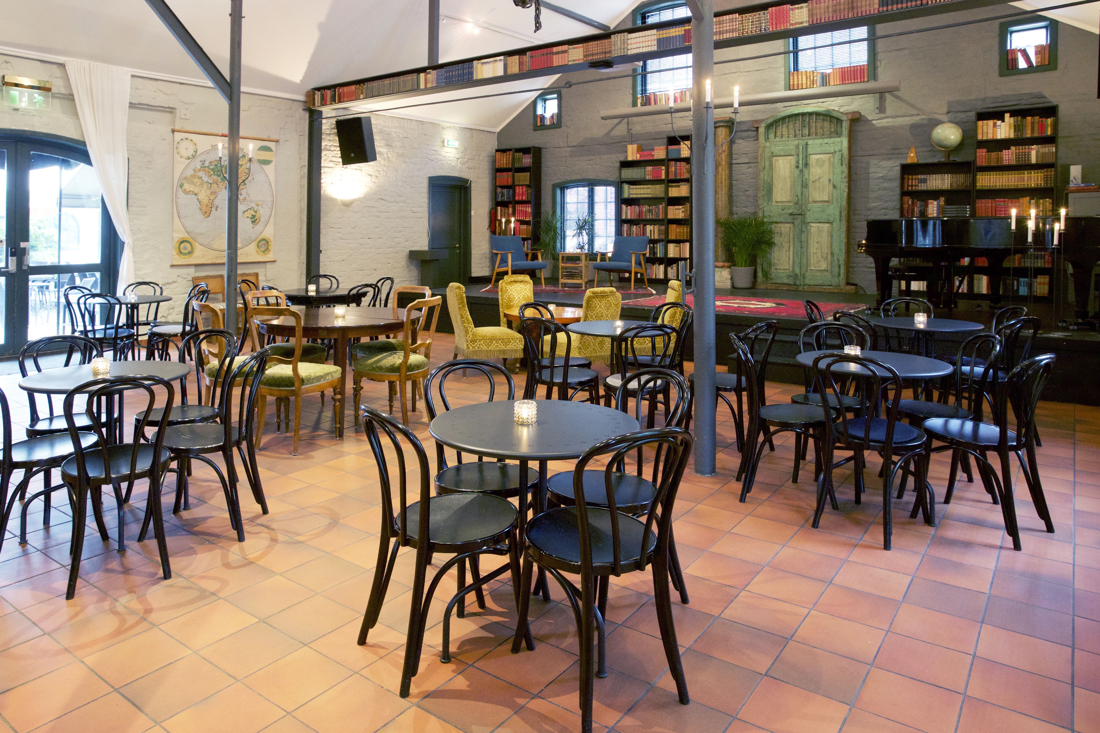 A library with multiple tables and chairs, bookshelves, and a piano.