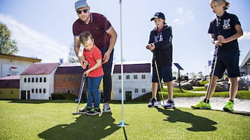 Un grupo de personas jugando al golf en un campo verde con edificios al fondo.