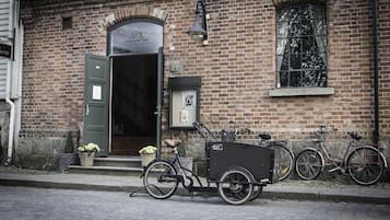 A brick building with a green door, a bicycle with a cargo box, and another bicycle leaning against the wall.