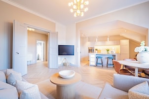 Una sala moderna con televisor, un comedor con mesa y sillas, y una cocina al fondo.