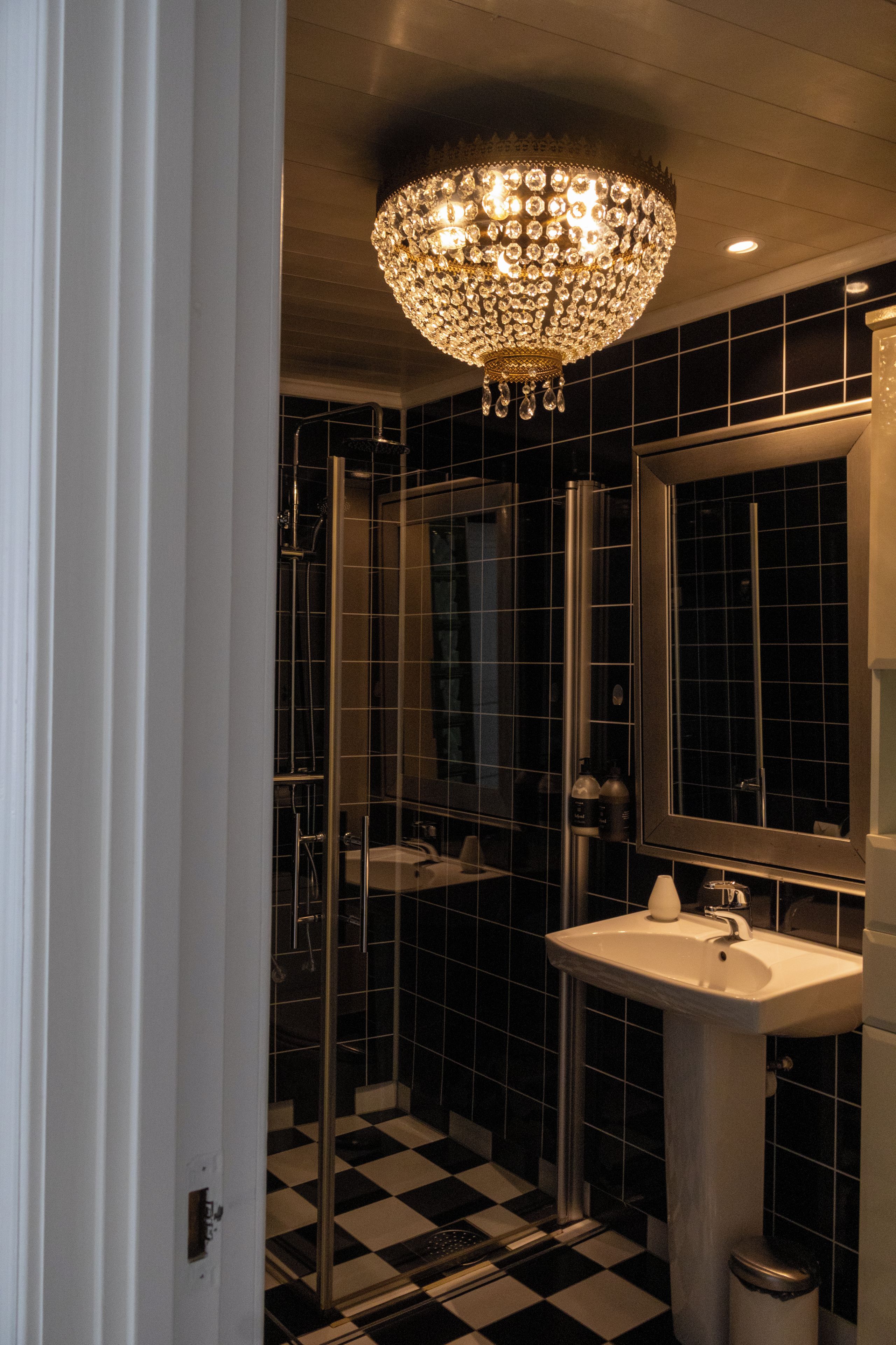 Un baño con piso a cuadros blanco y negro, un lavamanos blanco y un espejo grande.