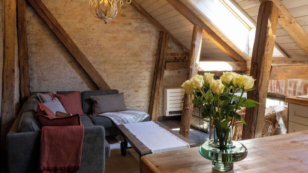 Habitació d'estil loft amb sostre de fusta, un candelabrum, un sofà, una taula i un ram de flors.