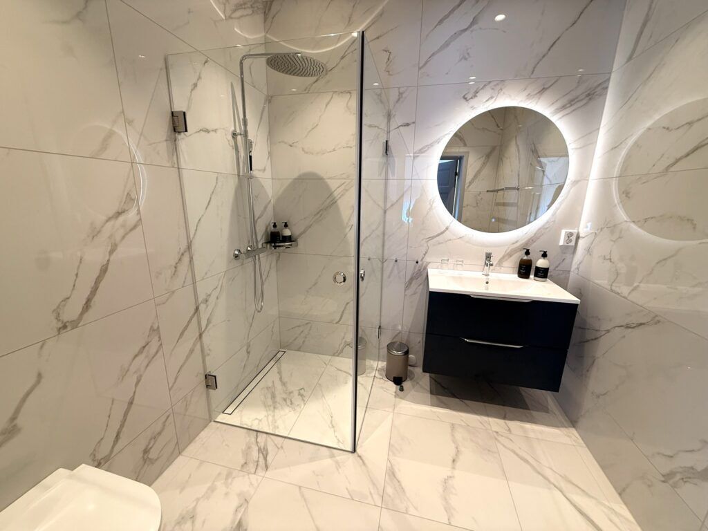 A modern bathroom with a glass-enclosed shower, a round mirror, and a dark-colored vanity.
