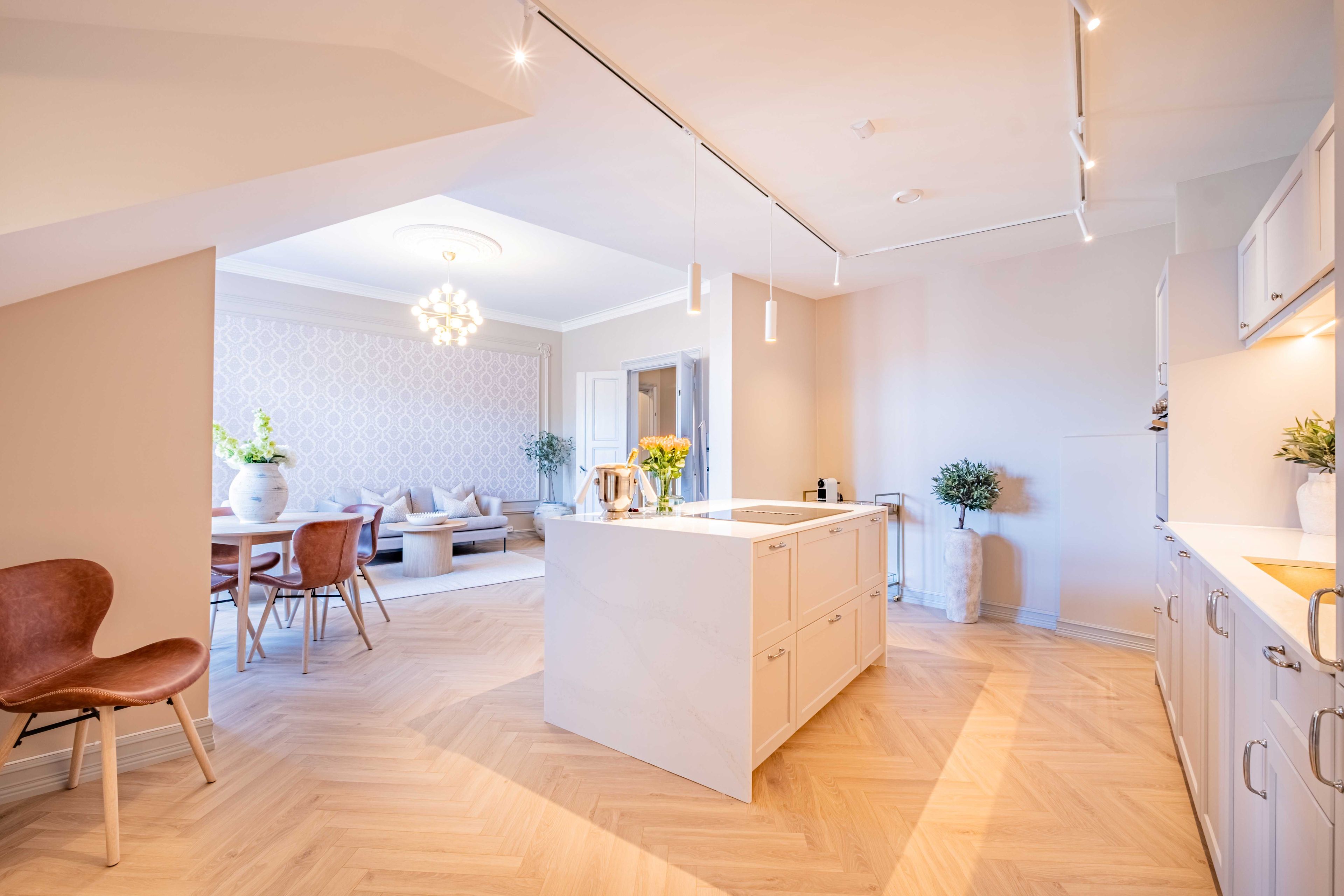 A modern kitchen with a central island, wooden flooring, and white cabinetry.