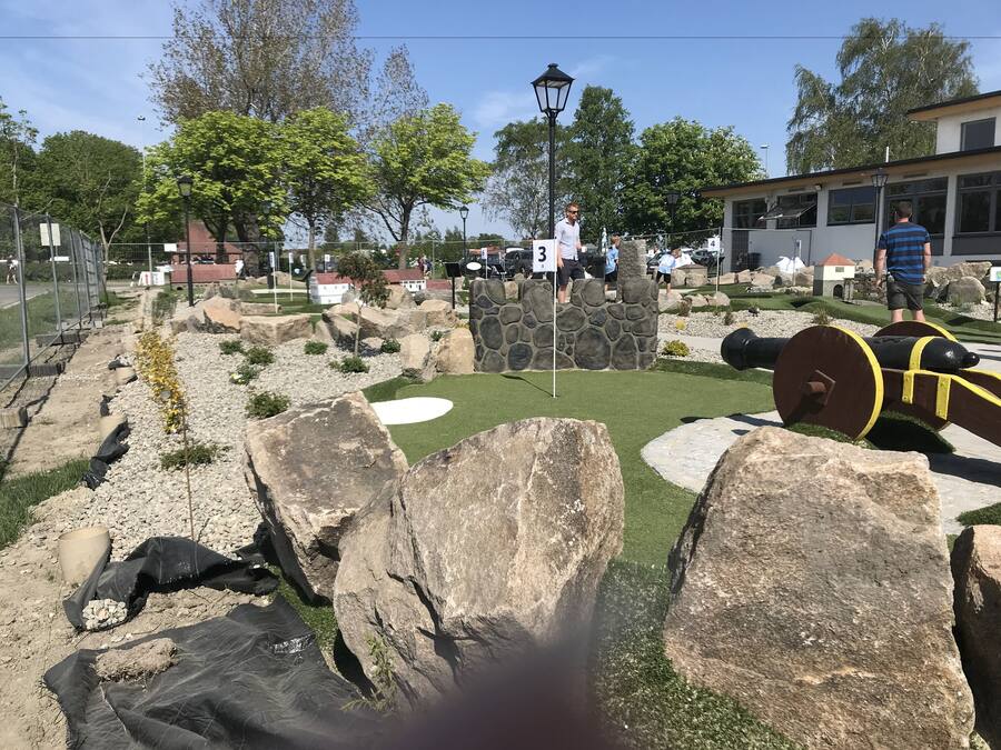 Un parcours de minigolf avec un mur en pierre, un canon et un drapeau.