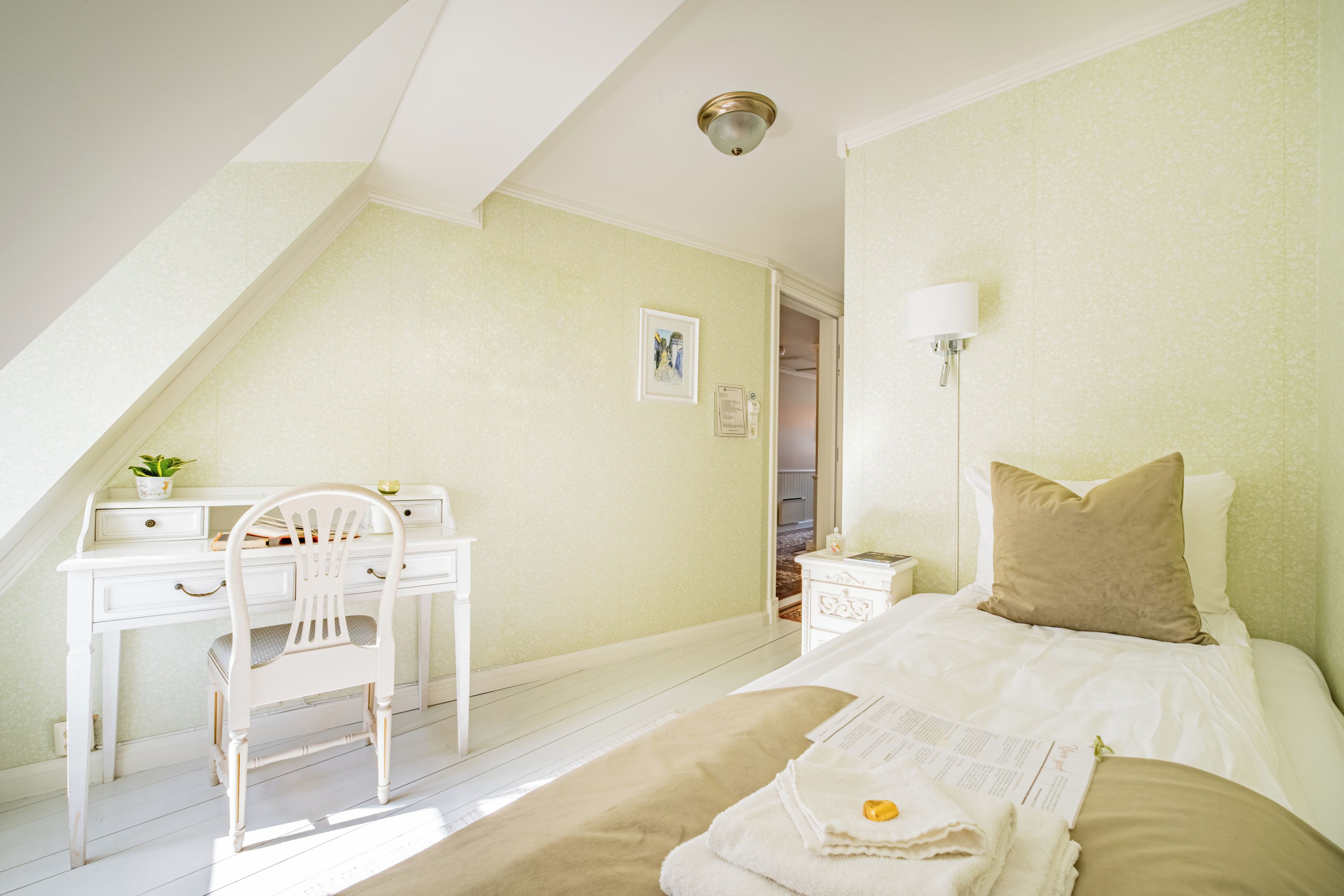 A bedroom with a bed, a desk, and a chair. There is a window providing natural light.