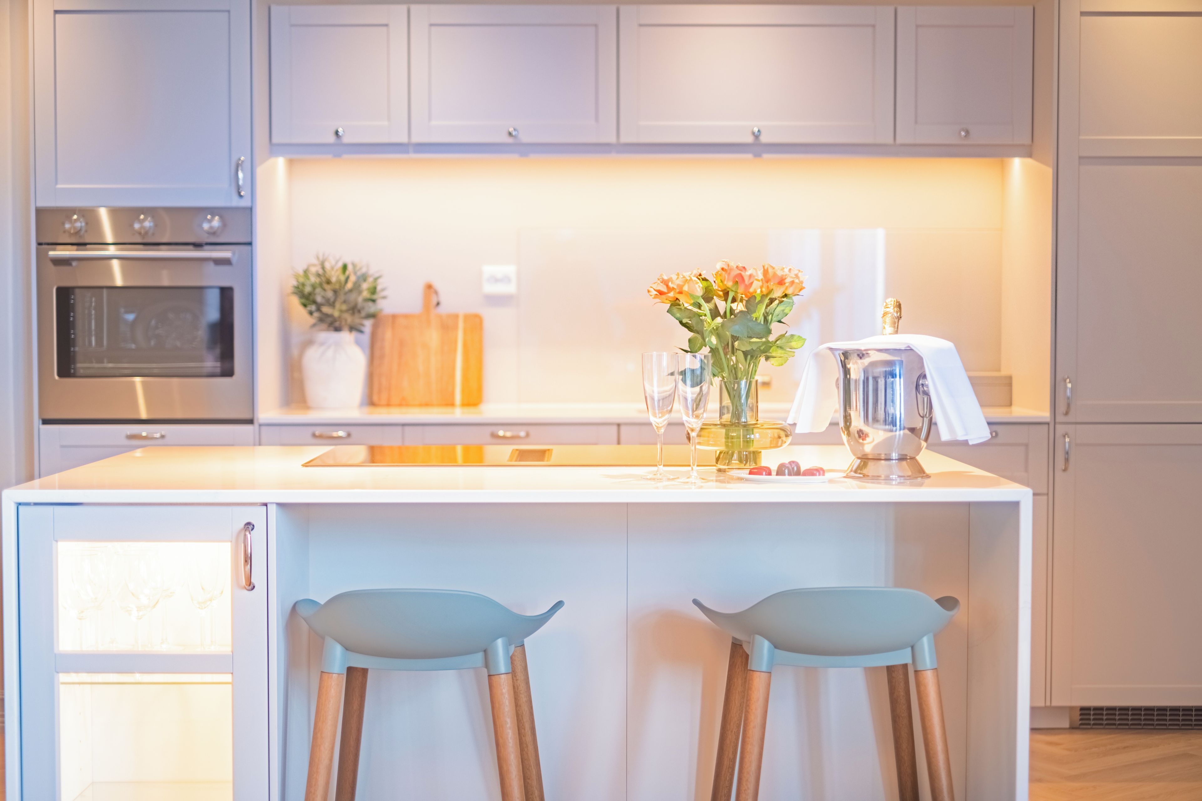 Una cocina moderna con una isla central, taburetes de bar, horno empotrado y una planta en maceta.