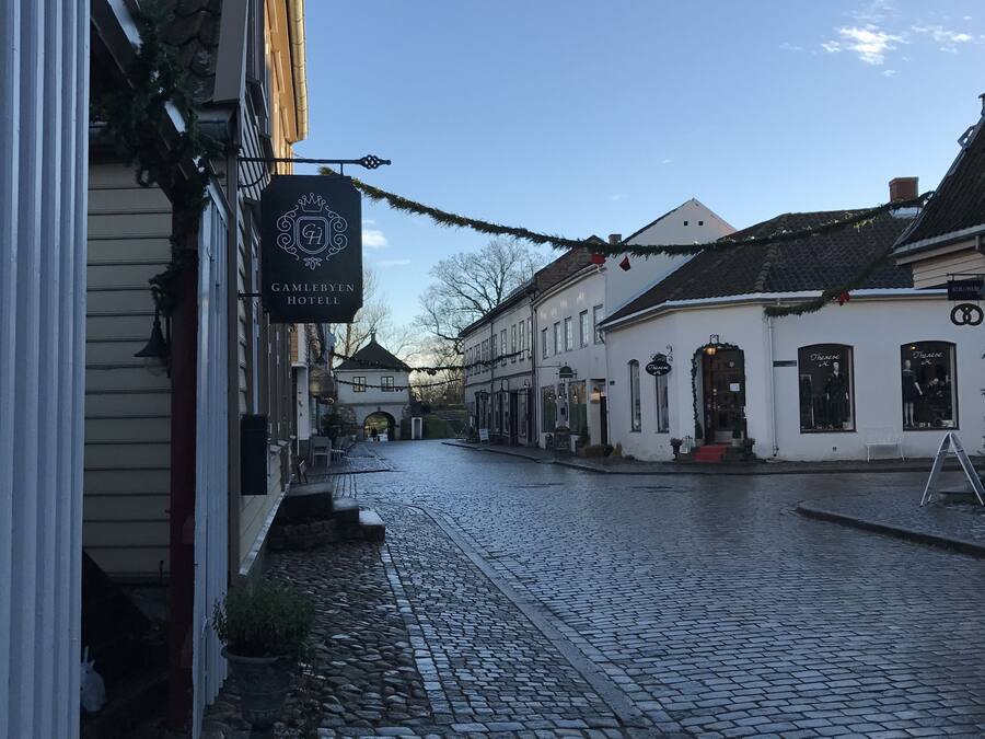 A cobblestone street lined with traditional buildings, including a hotel with a sign reading "Gamlebyen Hotel."